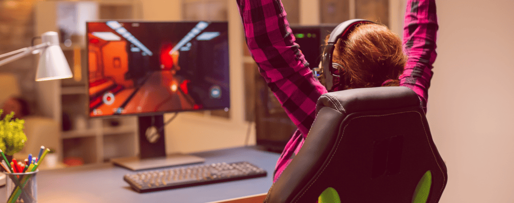 Mulher ruiva e de camisa xadrez comemorando sua vitória em um jogo online no computador