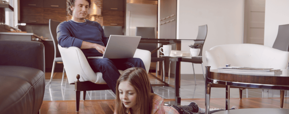 Foto de pai e filha utilizando seus gadgets conectados à internet na sala de sua casa
